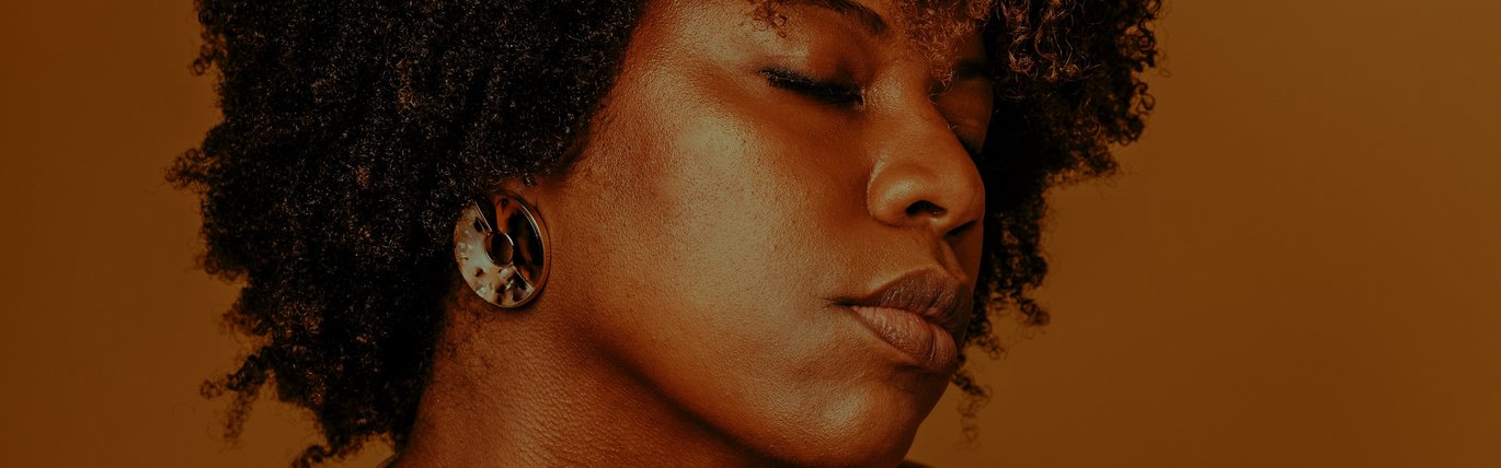 A black woman has her eyes closed and her arm wrapped around her body.