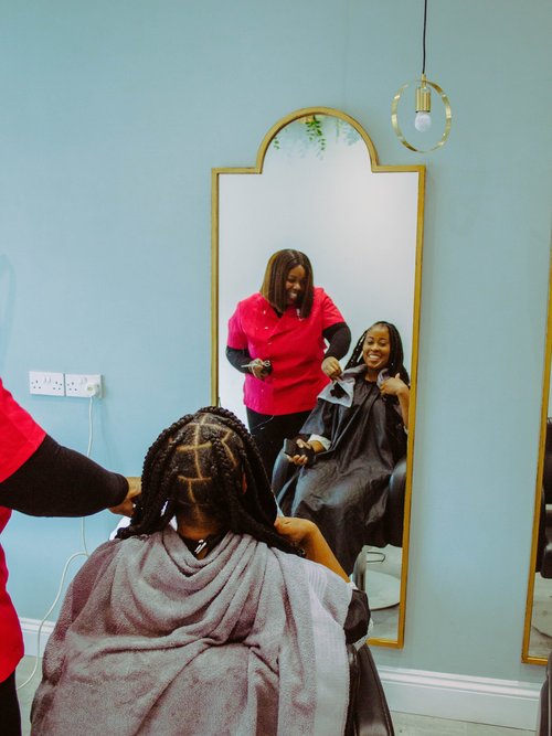 Woman looks into mirror at her braided style. Hairdresser is standing over her shoulder. Both of them are smiling.