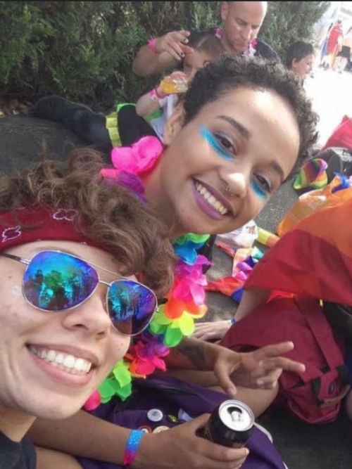 An image of Nic and a friend with glitter on their faces and bright flowers around their necks at Bristol PRiIDE