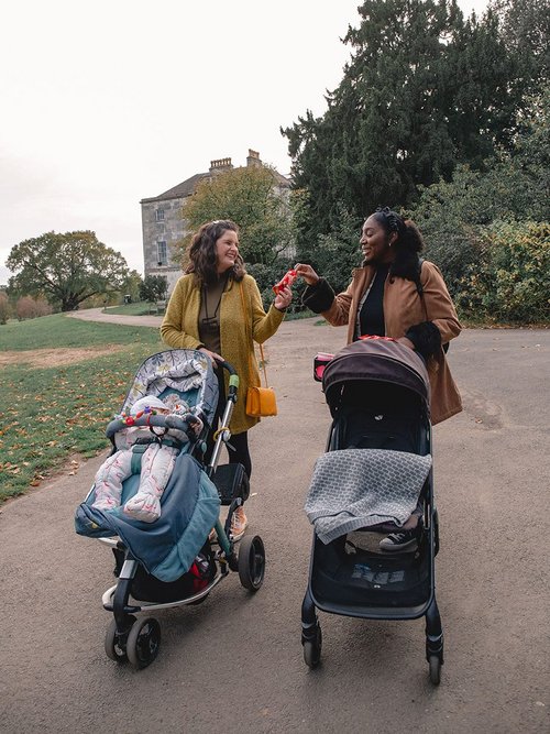 Two mums pushing buggies, sharing a bag of Maltesers