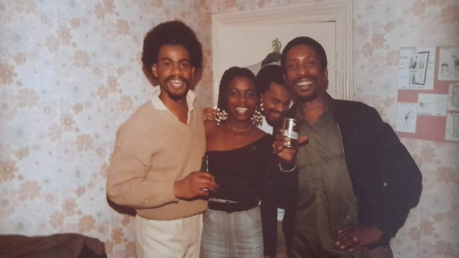 Everine stands in the centre of a group of friends, posing for the camera and holding up drinks