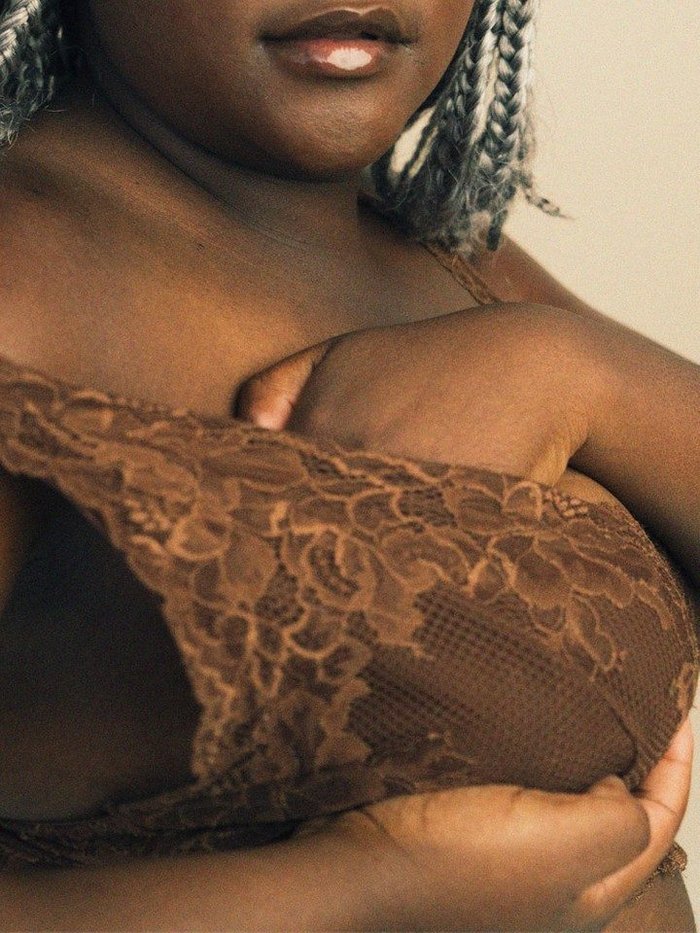A black woman is self-checking her breast in her brown lace bra.