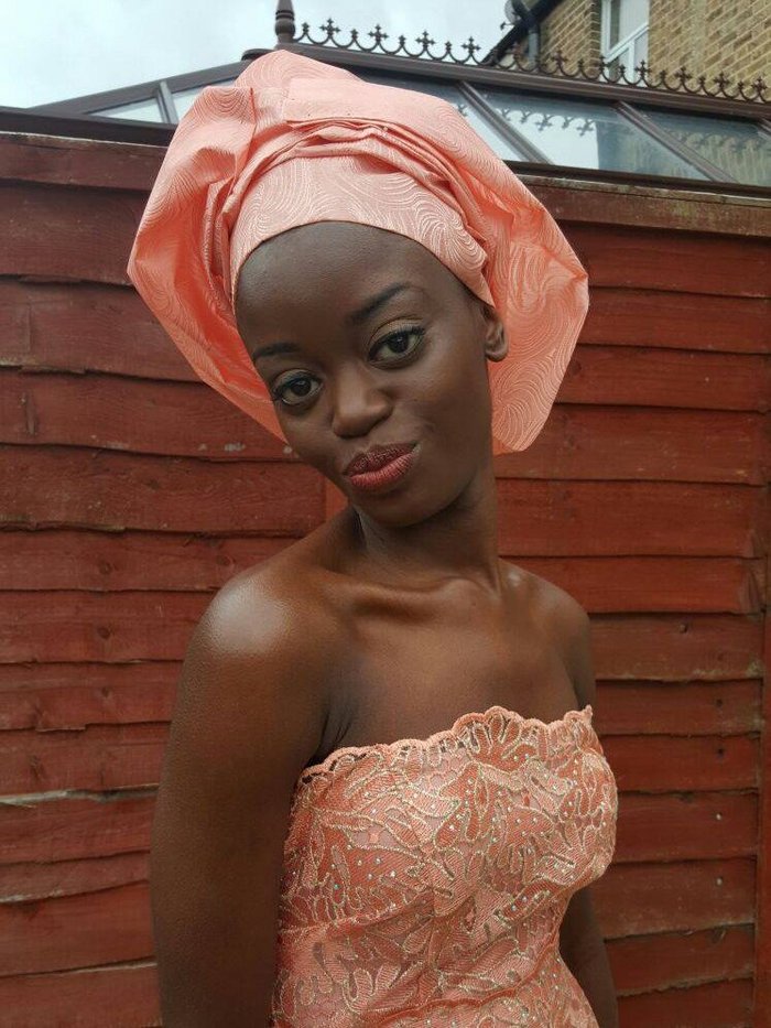 Isha poses wearing a coral pink lace dress with matching gele.