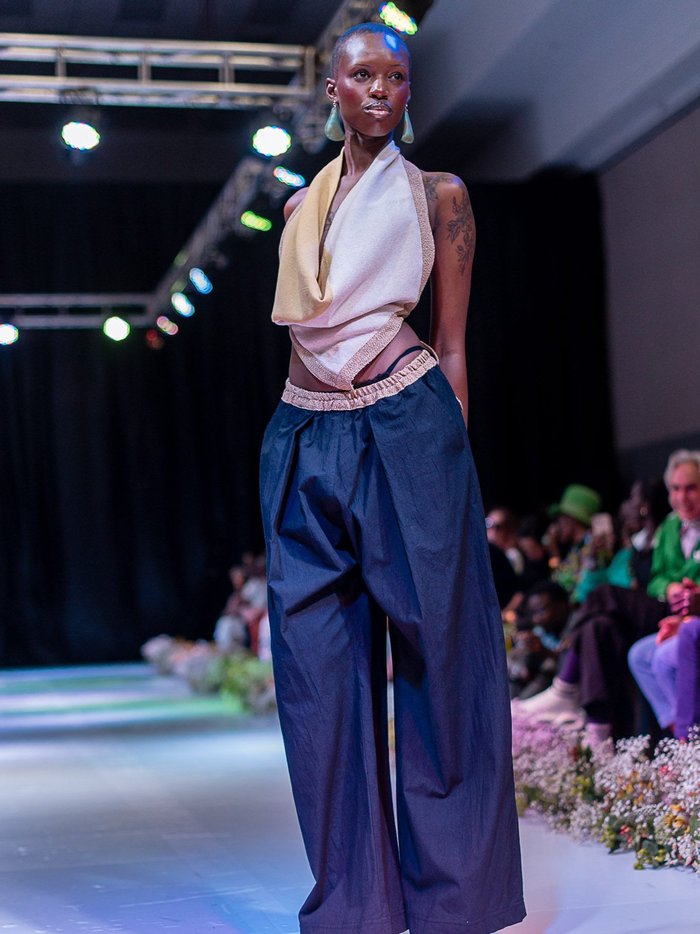Black model wearing loose fit dark trousers and a beige-toned handkerchief halter top.