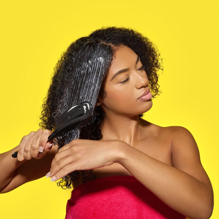 Black woman wrapped in a pink towel detangles her hair