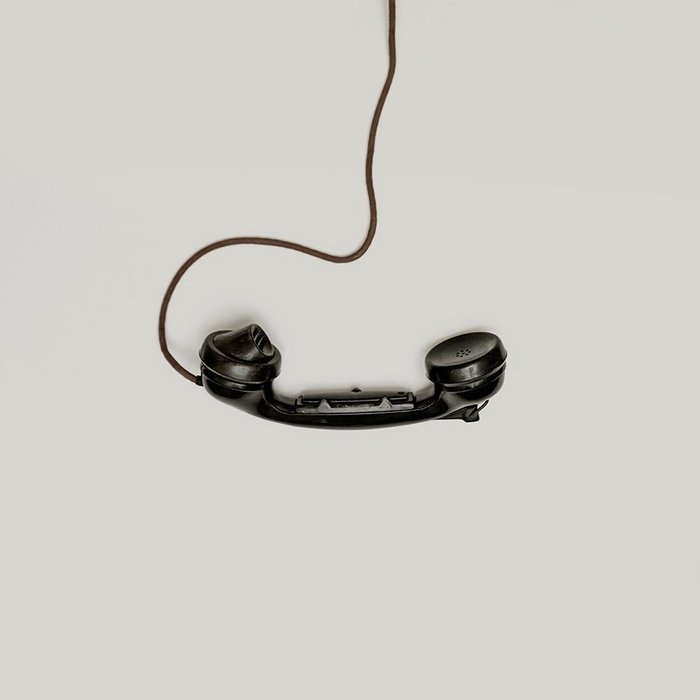 Black corded rotary phone receiver on a beige background.