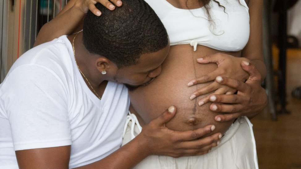 Man bending to kiss his partner's pregnant belly