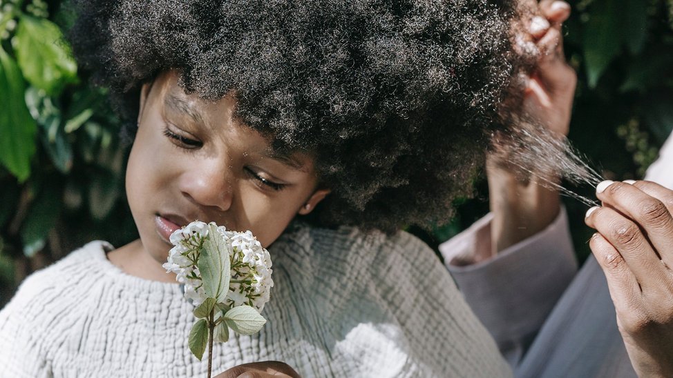 Small black girl with a large afro smells a flower.
