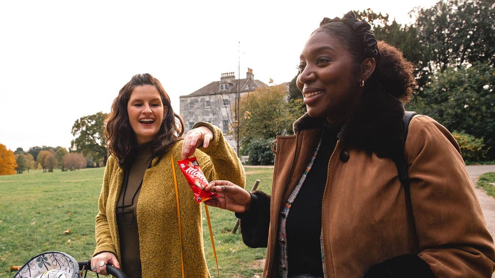 Samantha and Tash walking in the park with their buggies share some Maltesers