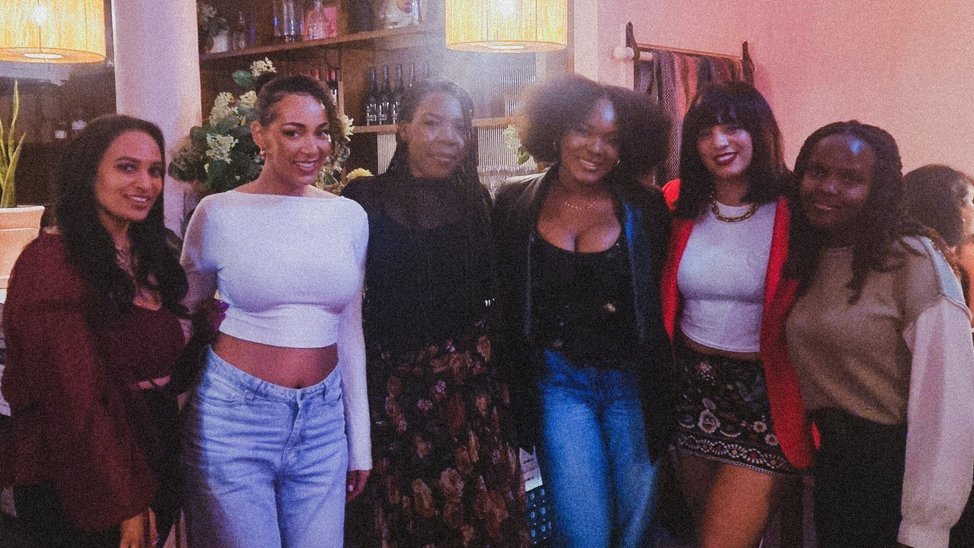 A group of black women, some mixed race, stand together and pose for a picture inside a bar.